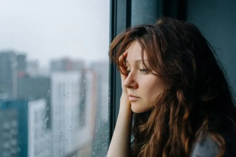 Young woman resting her chin on her hand while looking out a rain-streaked window