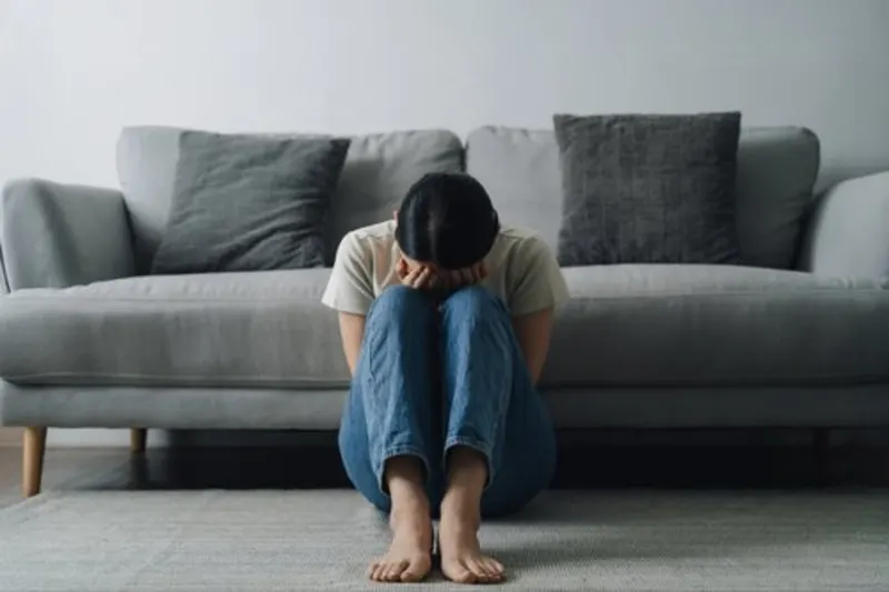 Person sitting on the floor with their head down, leaning against a couch