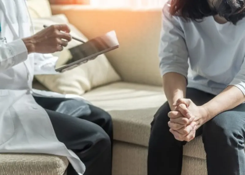Clinician holding a tablet while talking with a patient whose hands are clasped