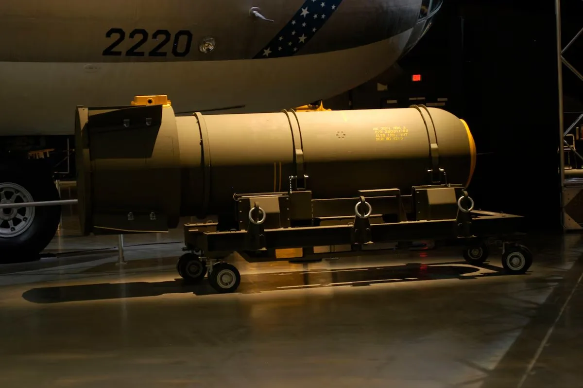 Bomba nuclear cilíndrica sobre un carrito con ruedas bajo un bombardero marcado con el número 2220 en un hangar de museo