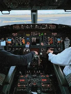 Two crew members' hands on the throttle quadrant and control column, runway visible ahead