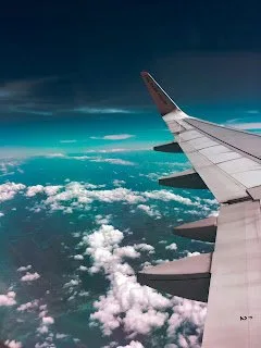 Airliner wing seen from a cabin window above scattered clouds