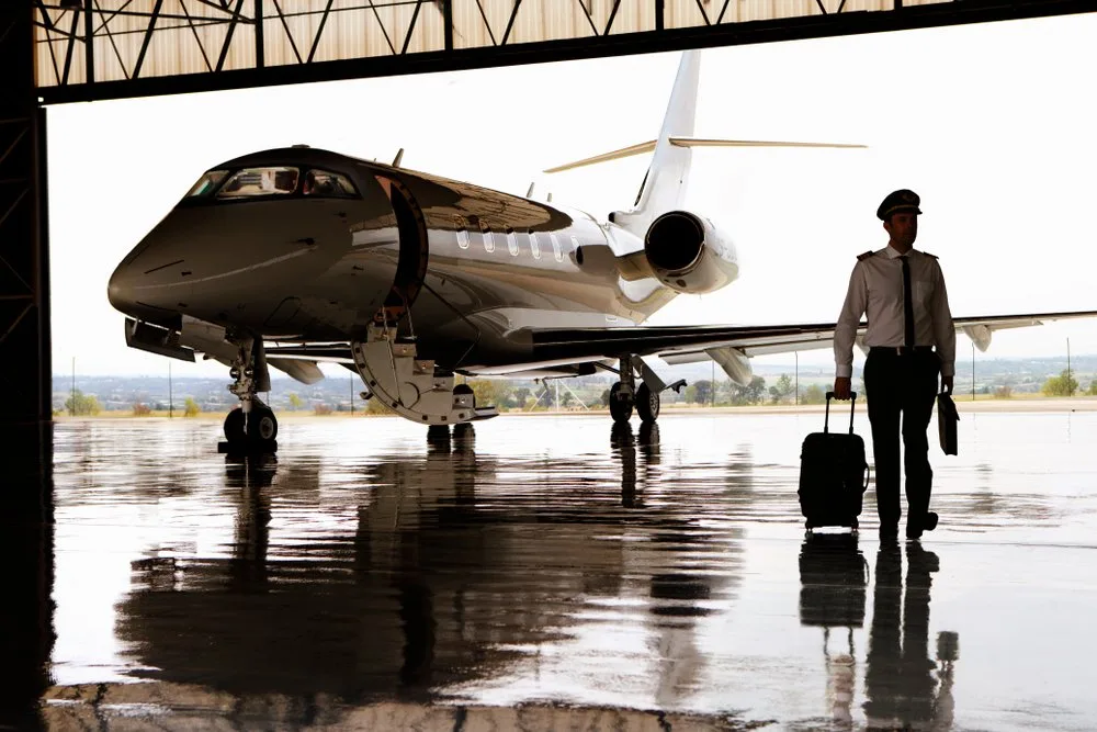 A pilot walking across a wet hangar floor towards a private jet under bright lighting in Vancouver, WA.